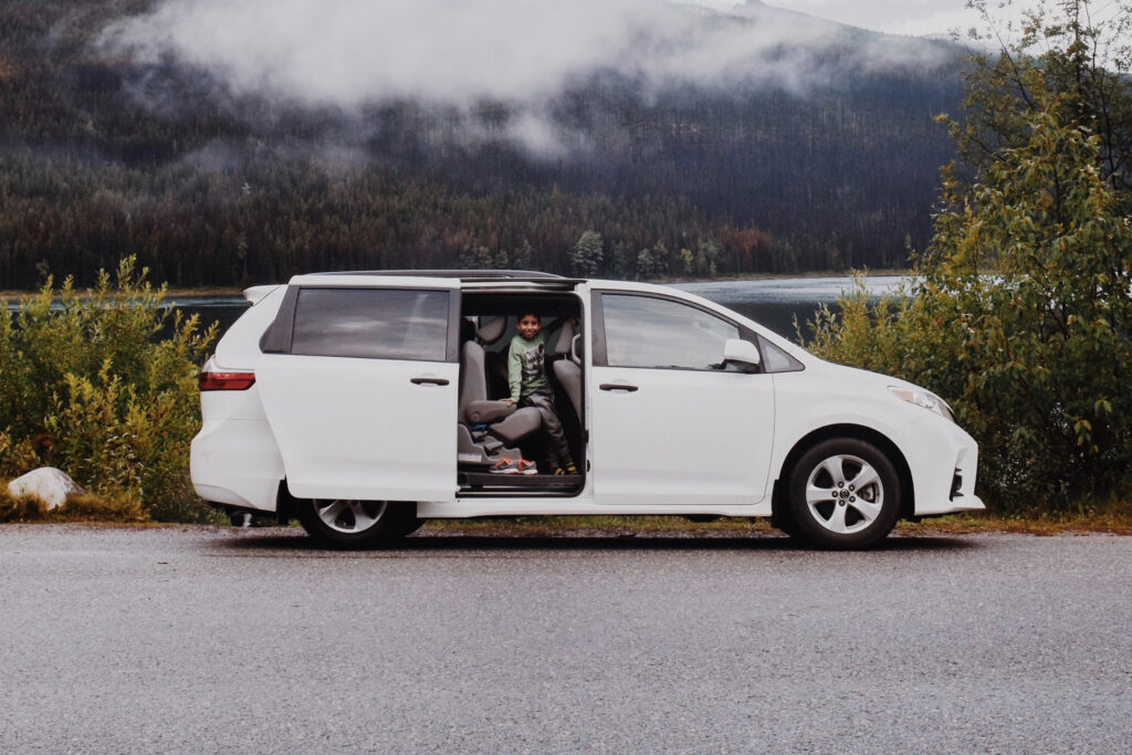 Biały minivan Toyota Sienna z otwartymi drzwiami na tle jeziora i gór