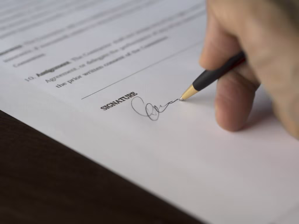 Dłoń podpisuje dokument długopisem na linii oznaczonej podpisem