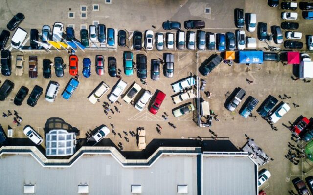 Widok z drona na zatłoczony parking z samochodami i ludźmi podczas plenerowego zlotu aut