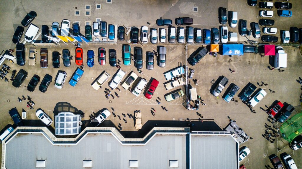 Widok z drona na zatłoczony parking z samochodami i ludźmi podczas plenerowego zlotu aut