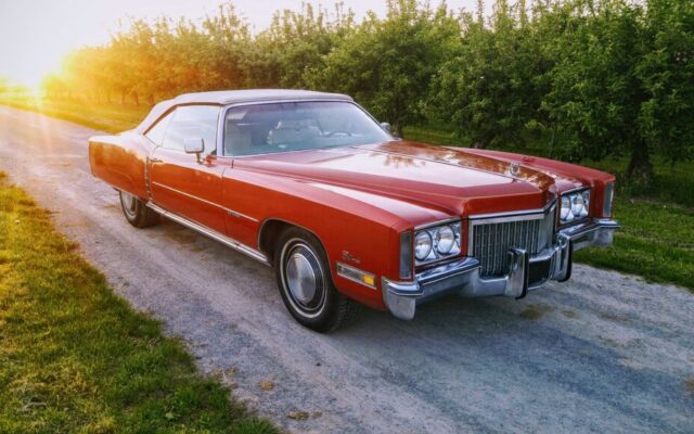 Czerwony klasyczny Cadillac cabrio stoi na szutrowej drodze przy sadzie o zachodzie słońca