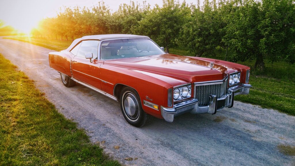 Czerwony klasyczny Cadillac cabrio stoi na szutrowej drodze przy sadzie o zachodzie słońca