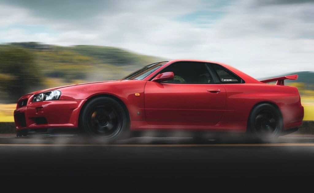 Czerwony Nissan Skyline GT-R jedzie szybko po drodze, z rozmytym tłem i ruchem kół