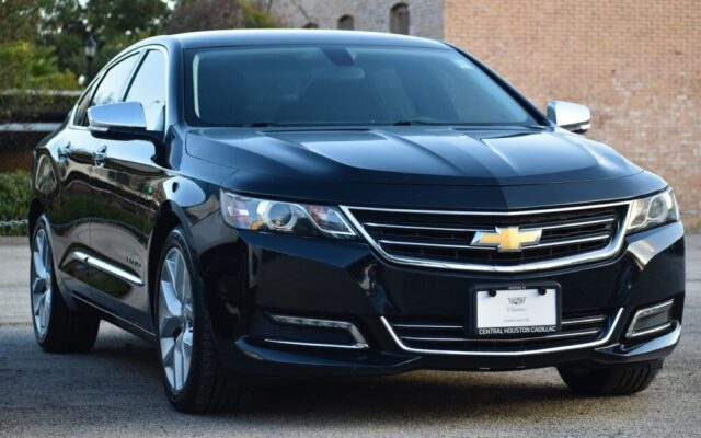 Czarny sedan Chevrolet Impala widziany z przodu na parkingu przy ceglanym budynku