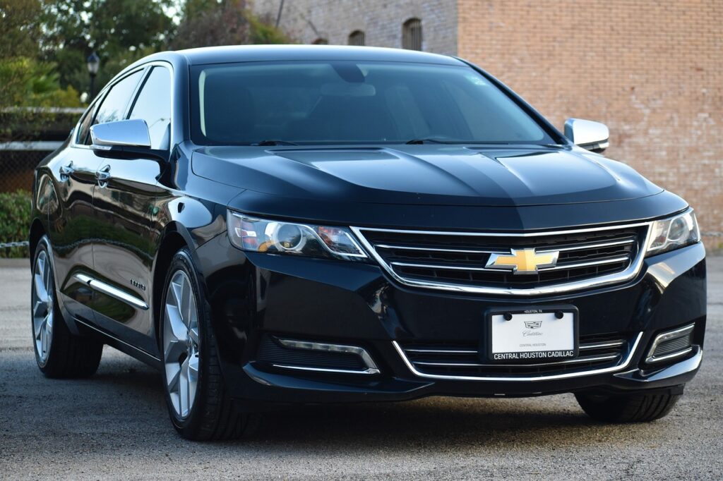 Czarny sedan Chevrolet Impala widziany z przodu na parkingu przy ceglanym budynku