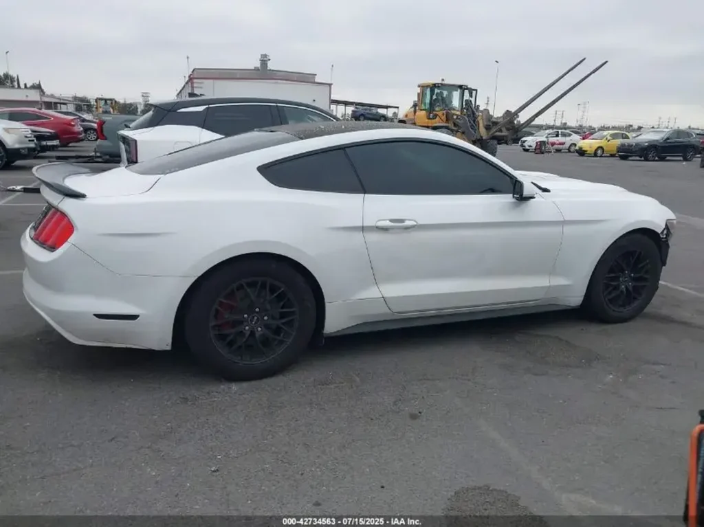 Biały Ford Mustang coupe stoi na placu aukcyjnym, widok z boku, z czarnymi felgami i ciemnymi szybami