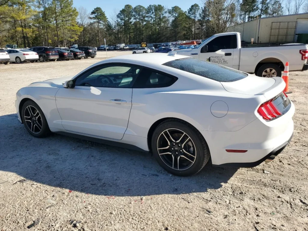 Biały Ford Mustang coupe widoczny z boku, zaparkowany na dużym parkingu.