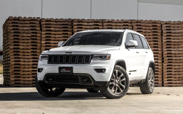 Biały Jeep Grand Cherokee zaparkowany przed stosami drewnianych palet na placu przemysłowym