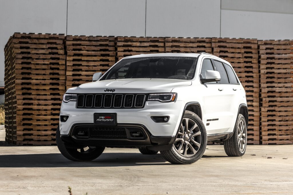 Biały Jeep Grand Cherokee zaparkowany przed stosami drewnianych palet na placu przemysłowym