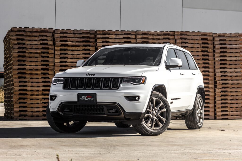 Biały Jeep Grand Cherokee, widok od przodu, na tle drewnianych palet w hali magazynowej.