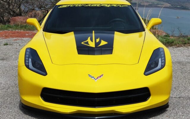 Żółty Chevrolet Corvette Stingray z czarną grafiką na masce, zaparkowany przy malowniczym punkcie widokowym