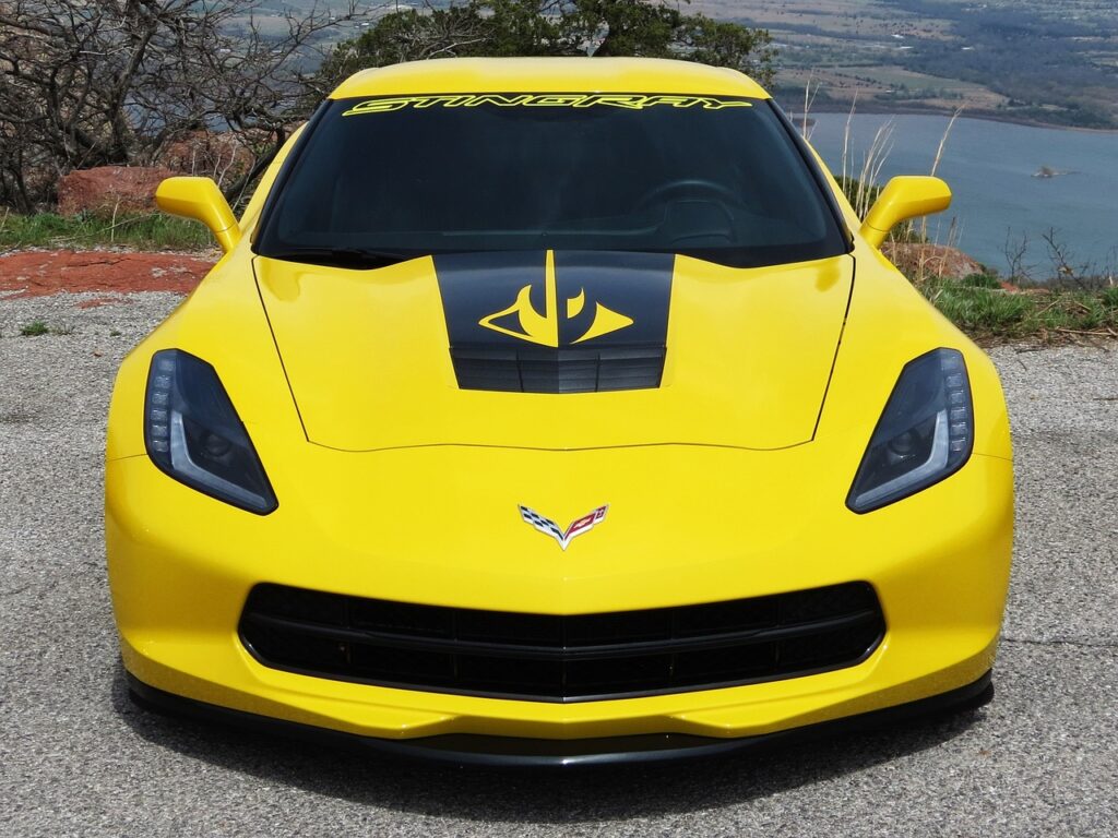 Żółty Chevrolet Corvette Stingray z czarną grafiką na masce, zaparkowany przy malowniczym punkcie widokowym