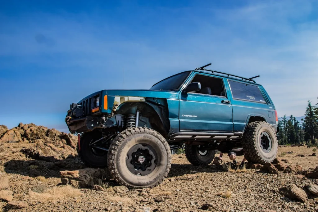 Niebieski Jeep Cherokee XJ z dużym prześwitem i terenowymi oponami podczas jazdy po skalistym terenie