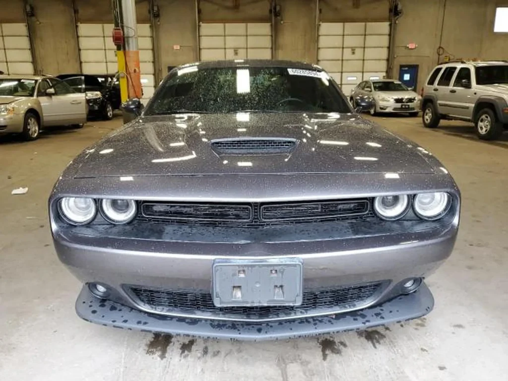 Przód szarego Dodge’a Challengera w hali, mokra karoseria i charakterystyczne podwójne okrągłe reflektory.