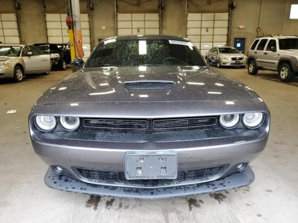 Przód szarego Dodge’a Challengera w hali, mokra karoseria i charakterystyczne podwójne okrągłe reflektory.