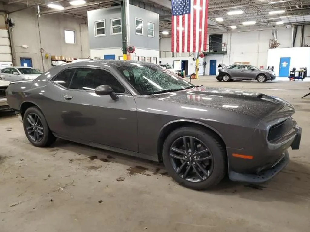 Szary Dodge Challenger coupe w hali, widok z przodu z lewej strony, w tle widoczna flaga USA.