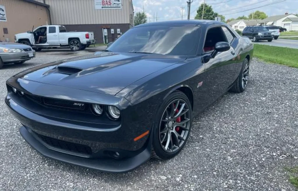 Czarny Dodge Challenger SRT stoi na żwirowym parkingu przed warsztatem samochodowym