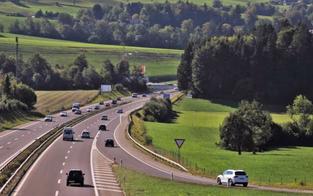 Samochody jadą krętą drogą przez zielone wzgórza i lasy na wiejskim terenie