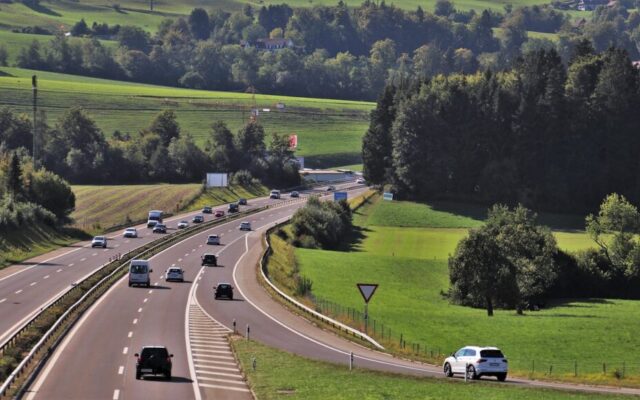 Samochody jadą krętą drogą przez zielone wzgórza i lasy na wiejskim terenie