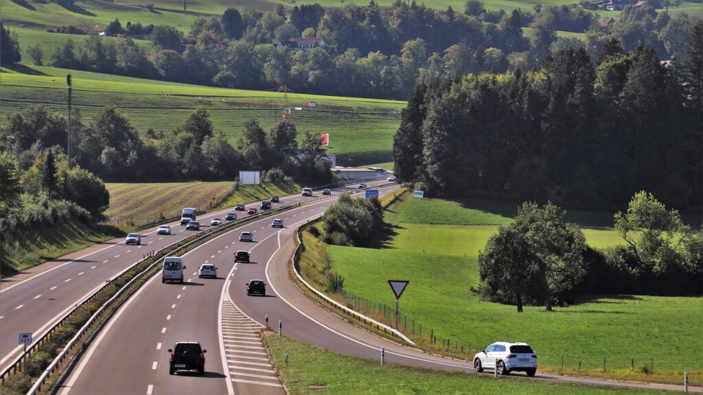 Samochody jadą krętą drogą przez zielone wzgórza i lasy na wiejskim terenie