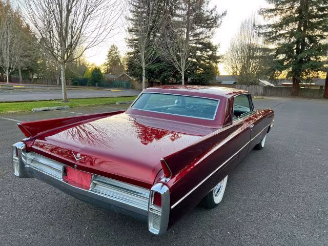 Bordowy Cadillac coupe od tyłu, długie płetwy i chromowane zderzaki, spokojny plener.