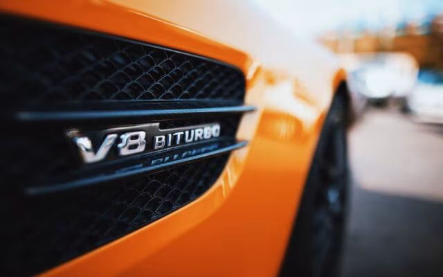Zbliżenie emblematu V8 Biturbo na bocznym wlocie powietrza pomarańczowego auta sportowego