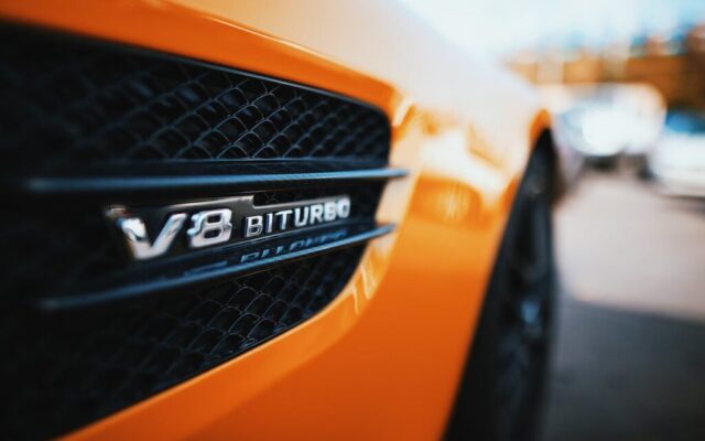 Zbliżenie emblematu V8 Biturbo na bocznym wlocie powietrza pomarańczowego auta sportowego