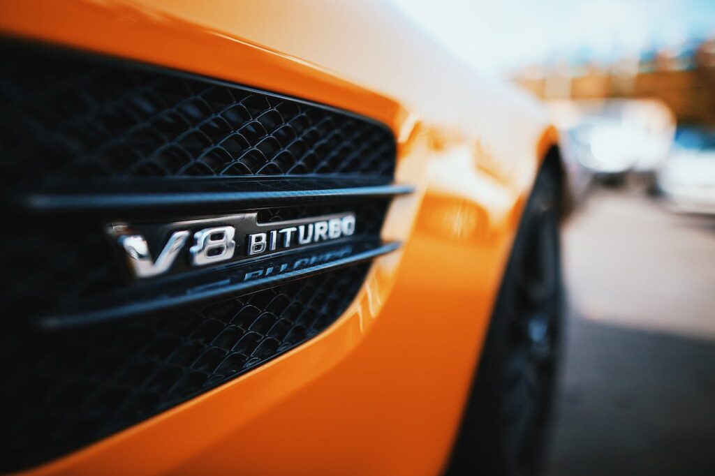 Zbliżenie emblematu V8 Biturbo na bocznym wlocie powietrza pomarańczowego auta sportowego