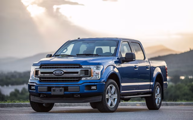 Niebieski pickup Ford F-150 zaparkowany na drodze z górskim krajobrazem w tle