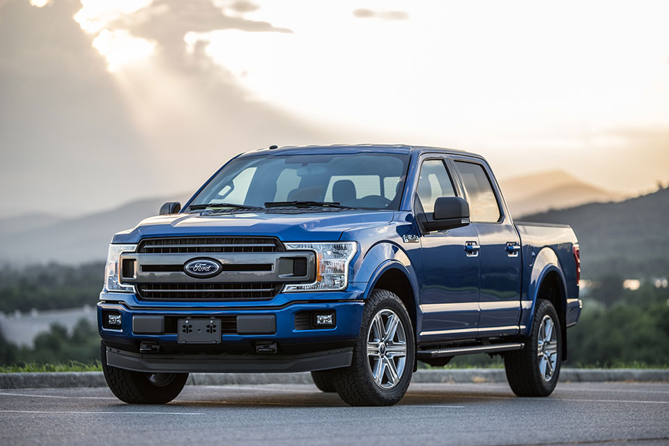Niebieski pickup Ford F-150 zaparkowany na drodze z górskim krajobrazem w tle