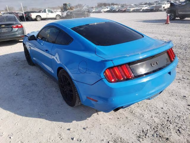 Niebieski Ford Mustang GT, tył-lewy rzut na żwirowym placu, przyciemnione szyby.