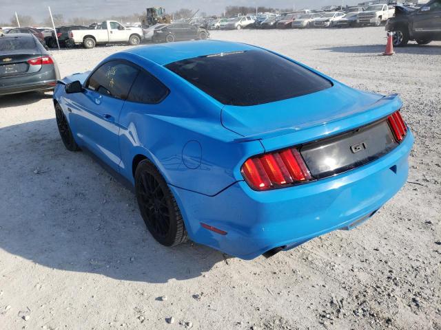 Niebieski Ford Mustang GT, tył-lewy rzut na żwirowym placu, przyciemnione szyby.