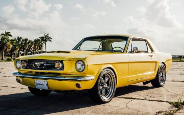 Żółty klasyczny Ford Mustang zaparkowany na betonowym placu pod palmami