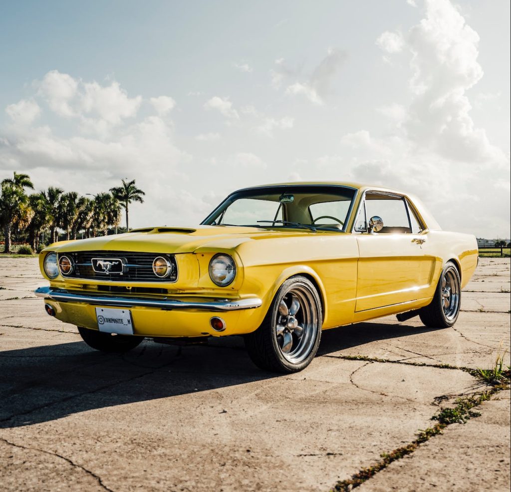Żółty klasyczny Ford Mustang zaparkowany na betonowym placu pod palmami