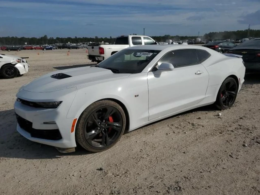 Białe coupe Chevrolet Camaro z czarnymi felgami stoi na żwirowym placu aukcji samochodowej