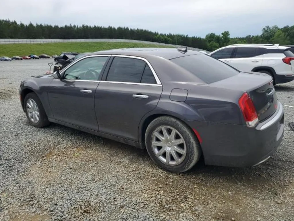 Szary Chrysler 300C uchwycony z tyłu pod kątem lewego boku; przyciemnione szyby i srebrne felgi, tło stanowi parking.