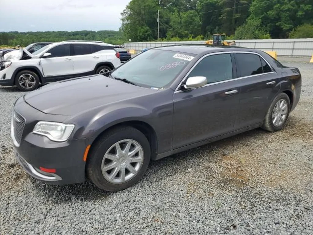 Szary Chrysler 300 stoi na żwirowym placu aukcyjnym z oznaczeniami na przedniej szybie