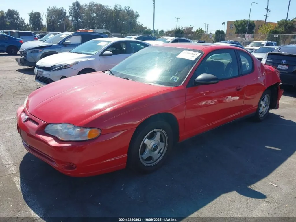 Czerwony Chevrolet Monte Carlo coupe, widok z przodu pod kątem lewym; auto stoi na parkingu, widoczne przetarcia i wgniecenie tylnego lewego błotnika.