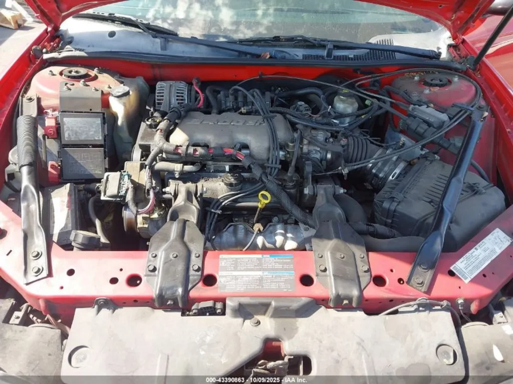 Komora silnika Chevrolet Monte Carlo z otwartą maską; widoczny osprzęt i wiązki, ogólne zabrudzenia eksploatacyjne.