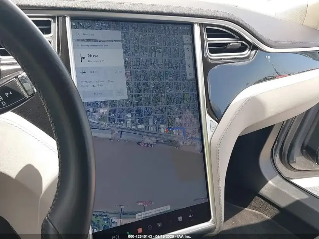 Wnętrze Tesli Model S; duży pionowy ekran z mapą nawigacji, fragment kierownicy i deski.