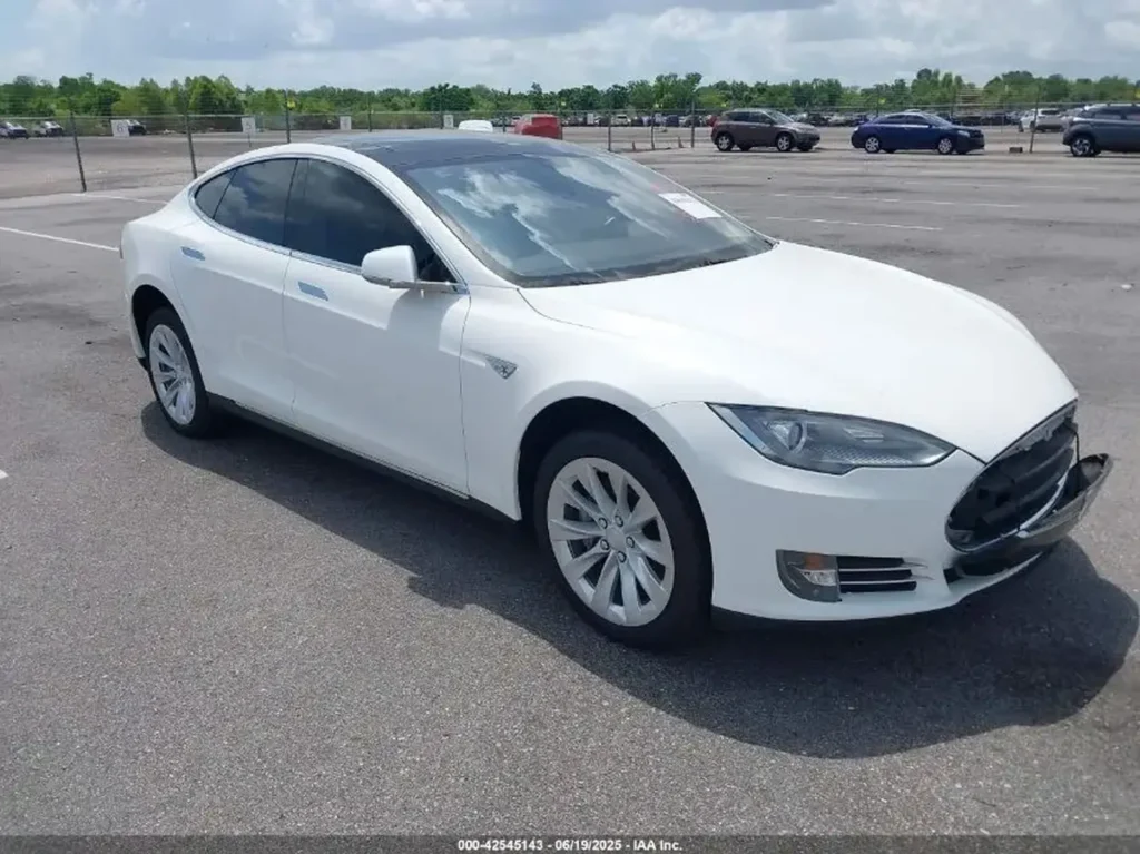 Biała Tesla Model S z lewej przodu na parkingu; brak przedniej kratki, przyciemnione szyby.