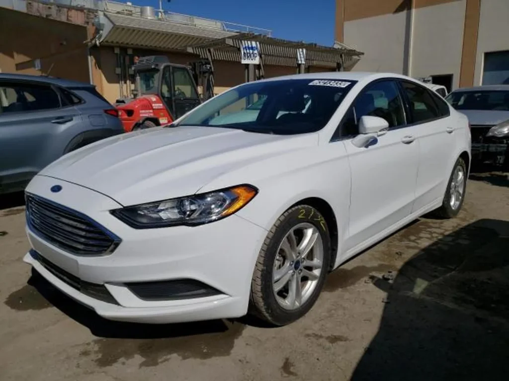 Biały Ford Fusion (2018) - widok z przodu/lewego boku na placu, reflektory LED i chromowany grill.