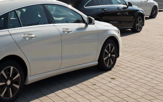 Biały sedan zaparkowany na brukowanym parkingu, z innymi samochodami w tle