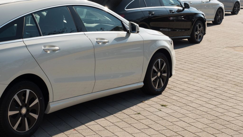 Biały sedan zaparkowany na brukowanym parkingu, z innymi samochodami w tle