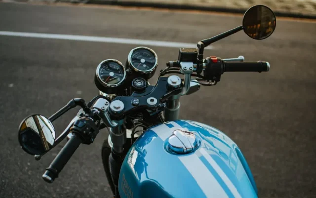 Kokpit niebieskiego motocykla z kierownicą, lusterkami i zegarami stojącego przy drodze