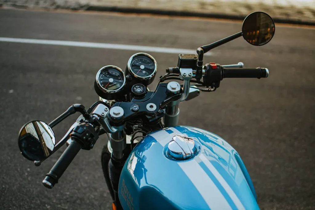 Kokpit niebieskiego motocykla z kierownicą, lusterkami i zegarami stojącego przy drodze