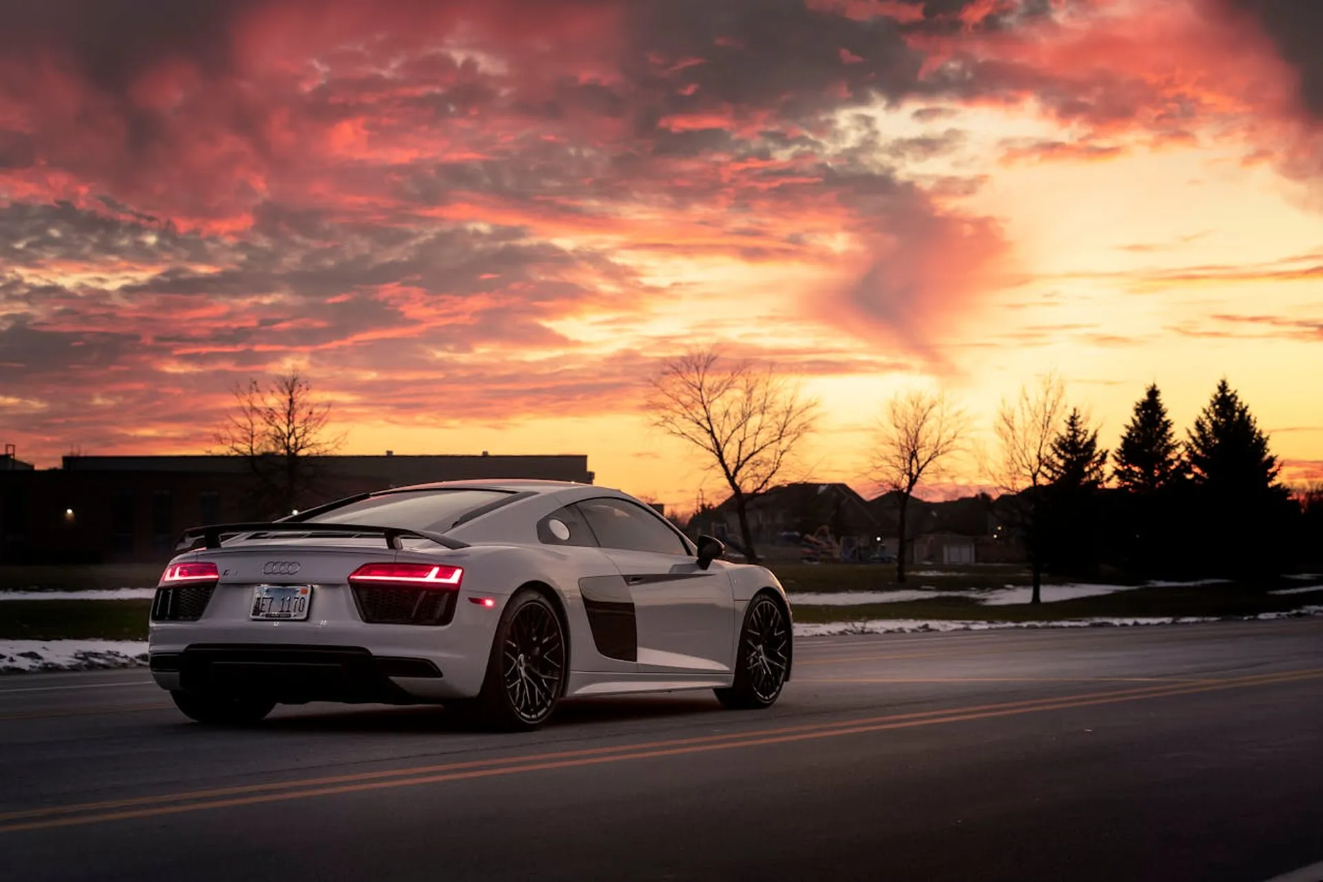 Białe Audi R8 stoi na drodze o zachodzie słońca, na tle zimowego krajobrazu i kolorowego nieba