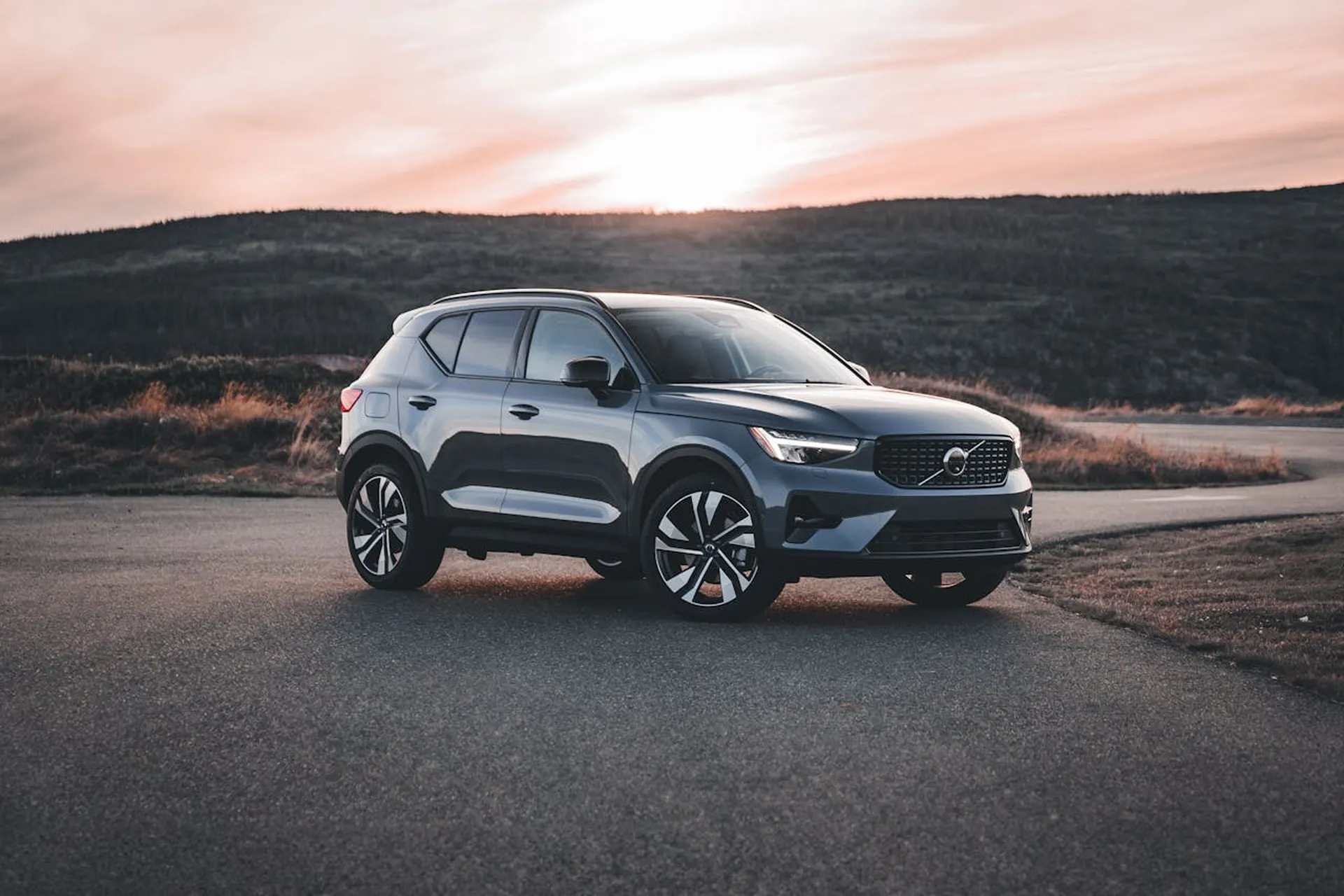 Volvo XC40 zaparkowane na asfaltowej drodze o zachodzie słońca, na tle leśnych wzgórz.
