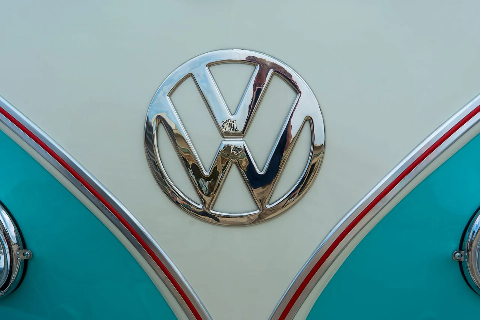 Chromowane logo Volkswagena na kremowo-niebieskiej karoserii klasycznego modelu, podkreślające retro stylistykę.