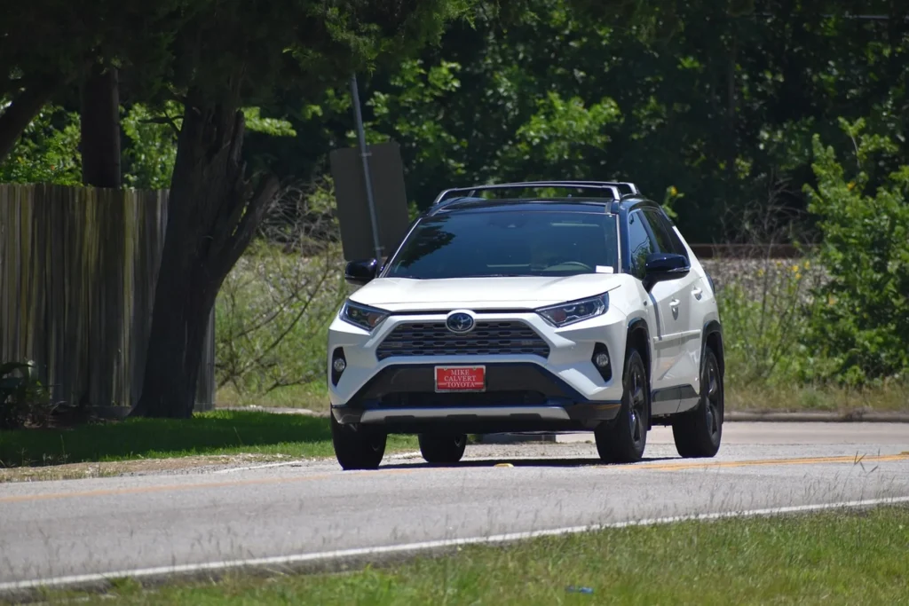 Biała Toyota RAV4 wersja amerykańska jadąca wiejską drogą w słoneczny dzień